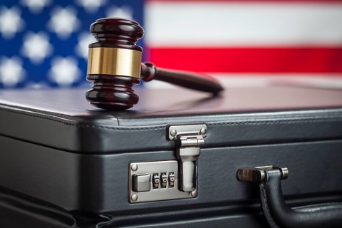 Leather briefcase and gavel resting on table with american flag behind