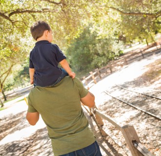 Happy mixed-race son enjoys a piggy back ride in the park with dad