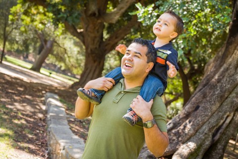 Happy mixed-race son enjoys a piggy back ride in the park with dad