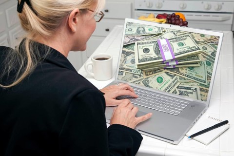 Woman in kitchen using laptop to earn or win money. screen can be easily used for your own message or picture. picture on screen is my copyright as well