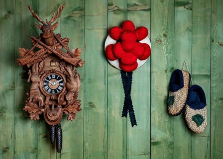 Black Forest cuckoo clock with Bollen hat and straw shoes in front of green wooden wall