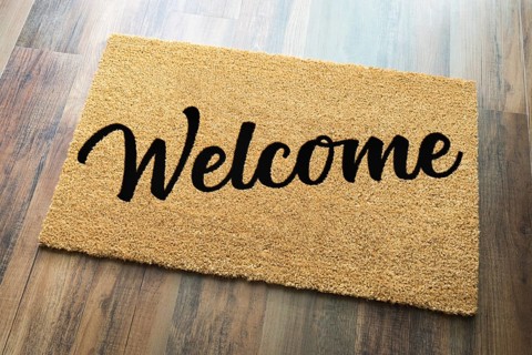 Tan welcome mat on wood floor background