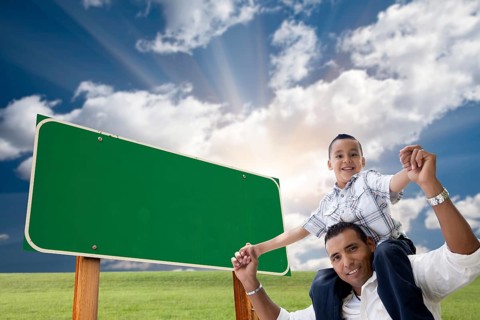Attractive happy hispanic father and son in front of blank green road sign ready for your own message