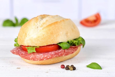 Roll sandwich baguette topped with salami ham on wooden board in Germany