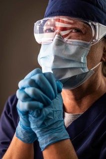 American flag reflecting on distressed praying female medical worker wearing protective face mask and goggles