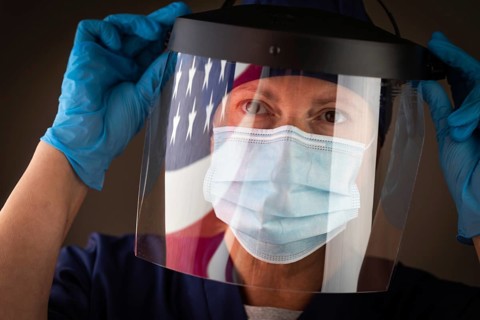 American flag reflecting on female medical worker wearing protective face mask and shield