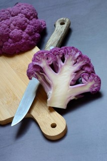 Halved purple cauliflower on wooden board with kitchen knife