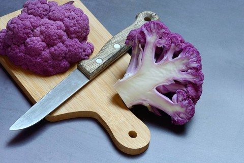 Halved purple cauliflower on wooden board with kitchen knife