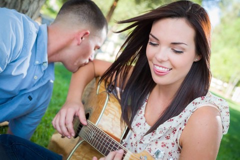 Happy mixed-race couple at the park playing guitar and singing songs