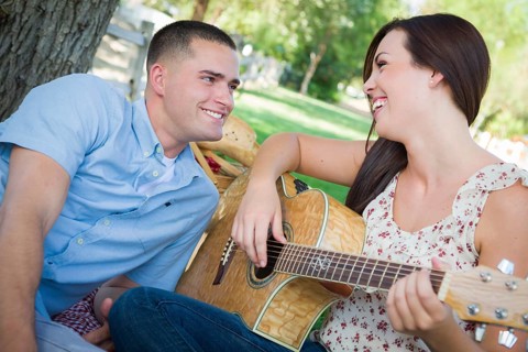 Happy mixed-race couple at the park playing guitar and singing songs