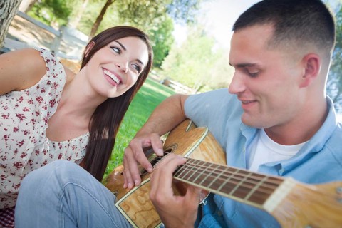 Happy mixed-race couple at the park playing guitar and singing songs