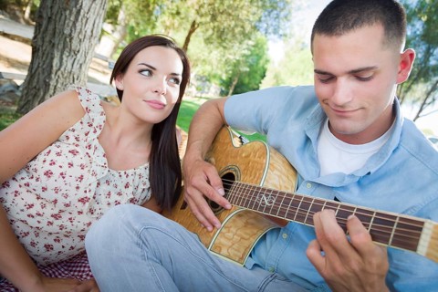 Happy mixed-race couple at the park playing guitar and singing songs
