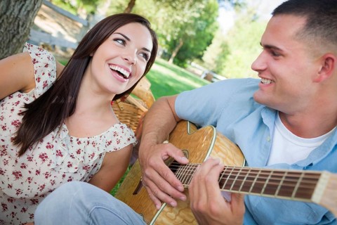 Happy mixed-race couple at the park playing guitar and singing songs