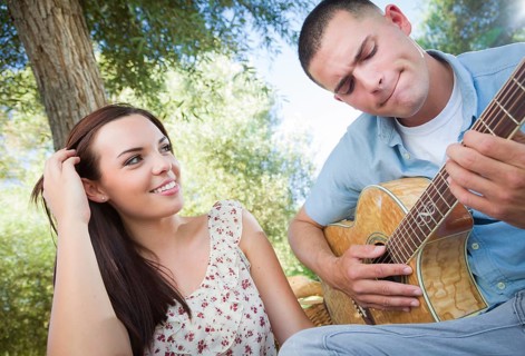 Happy mixed-race couple at the park playing guitar and singing songs