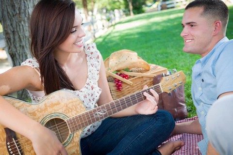 Happy mixed-race couple at the park playing guitar and singing songs