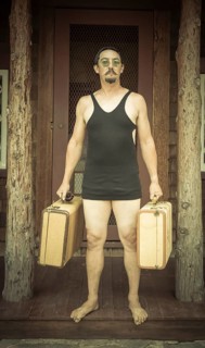 Goofy gentleman dressed in 1920's era swimsuit holding suitcases on porch of cabin