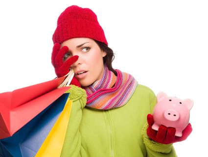 Concerned expressive mixed-race woman wearing winter clothing holding shopping bags and piggybank isolated on white background