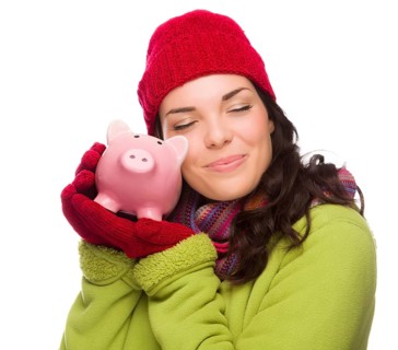 Pleased mixed-race woman wearing winter clothing hugging piggybank isolated on white background