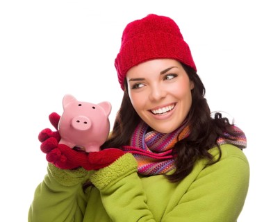 Happy mixed-race woman wearing winter clothing holding piggybank isolated on white background