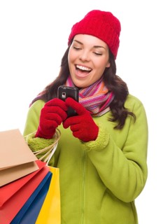mixed-race woman wearing winter clothing holding shopping bags texting on cell phone isolated on white background