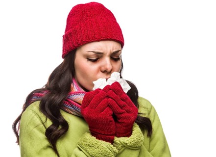 Sick mixed-race woman wearing winter hat and gloves blowing her sore nose with a tissue isolated on white background