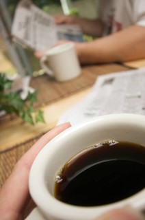 Morning coffee macro of cup with man reading newspaper in background