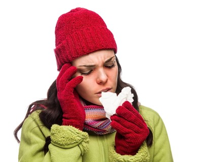 Sick mixed-race woman wearing winter hat and gloves blowing her sore nose with a tissue isolated on white background