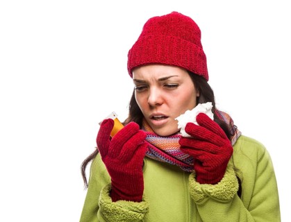 Sick mixed-race woman wearing winter hat and gloves blowing her sore nose and holding empty medicine bottle isolated on white
