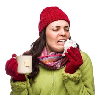 Sick mixed-race woman wearing winter hat and gloves blowing her sore nose and holding cup of hot tea isolated on white