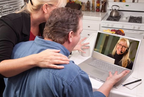 Couple in kitchen using laptop with customer support woman on the screen