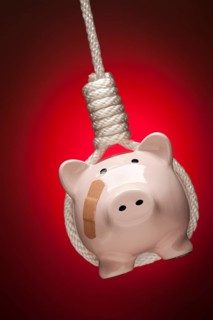 Piggy bank with bandage hanging in hangman's noose on red spot lit background