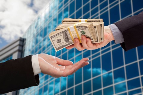 Male hand handing stack of cash to woman with corporate building