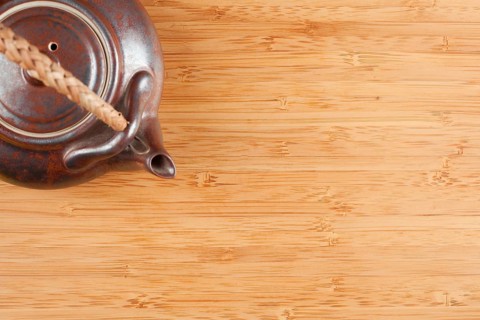 Tea pot and bamboo textured surface background with plenty of room for text