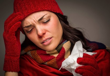 Sick mixed-race woman wearing winter hat and gloves blowing her sore nose with a tissue