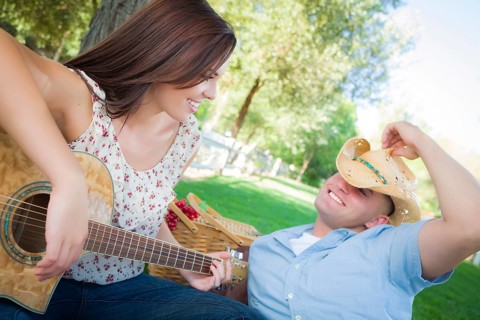 Happy attractive mixed-race couple with guitar and cowboy hat in the park