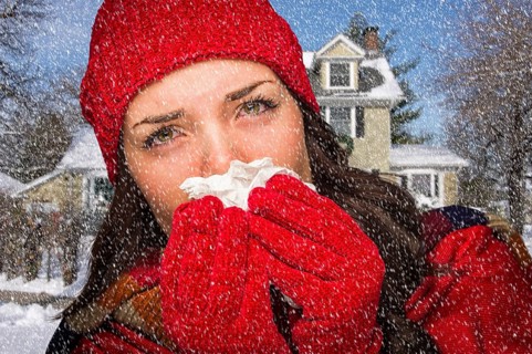 Miserable sick woman in falling snow blowing her sore nose with tissue outside
