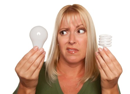 Funny faced woman holds energy saving and regular light bulbs isolated on a white background