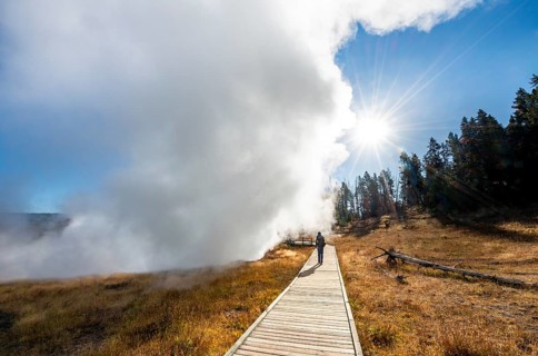 Hiker on footbridge next to steaming hot spring