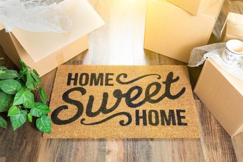 Home sweet home welcome mat and moving boxes on hard wood floor