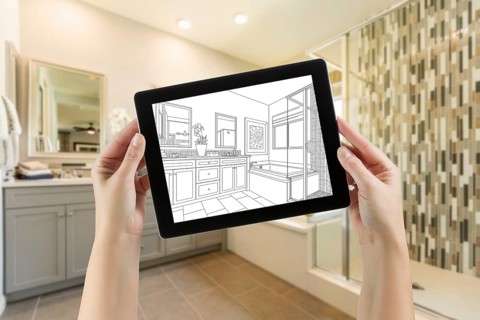 Hands holding computer tablet with master bathroom drawing on screen and photo behind