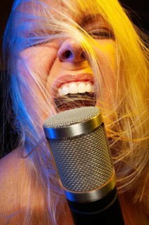 Female vocalist under gelled lighting sings with passion into condenser microphone