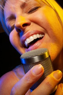 Female vocalist under gelled lighting sings with passion into condenser microphone