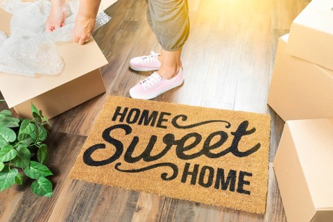 Woman in pink shoes and sweats unpacking near home sweet home welcome mat