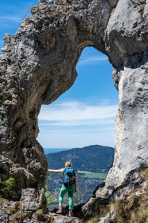 Hiker standing in the rock gate Breitensteinfensterl with view of high fog over the valley