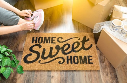 Woman wearing sweats and untying pink shoes near home sweet home welcome mat
