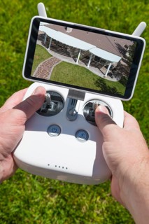 Hands holding drone quadcopter controller with overhead of house on screen