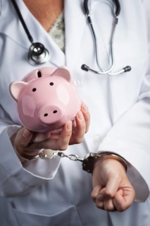 Female doctor or nurse in handcuffs holding piggy bank wearing lab coat and stethoscope