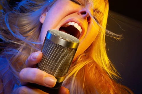 Female vocalist under gelled lighting sings with passion into condenser microphone