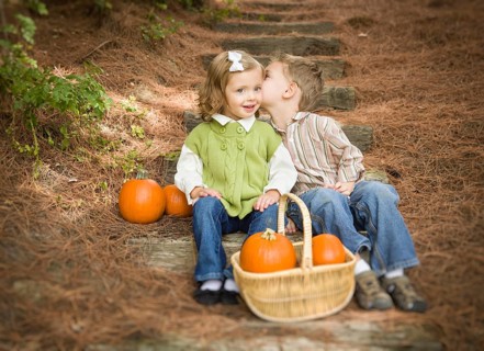 Adorable brother and sister children sitting on wood steps with pumpkins whispering secrets or kissing cheek