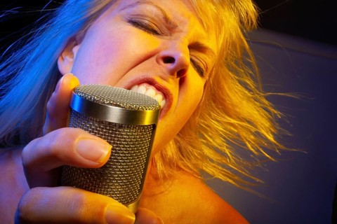 Female vocalist under gelled lighting sings with passion into condenser microphone